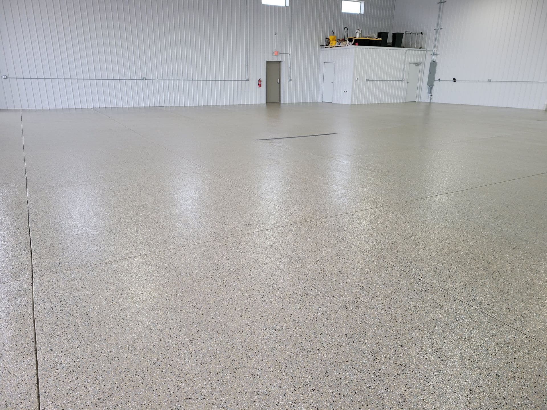 Spacious industrial interior with polished, speckled concrete floors and white corrugated metal walls. A small doorway and storage area are visible.